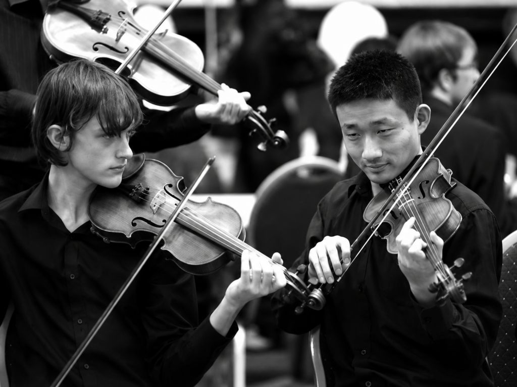 Two young string players perform in an orchestra.